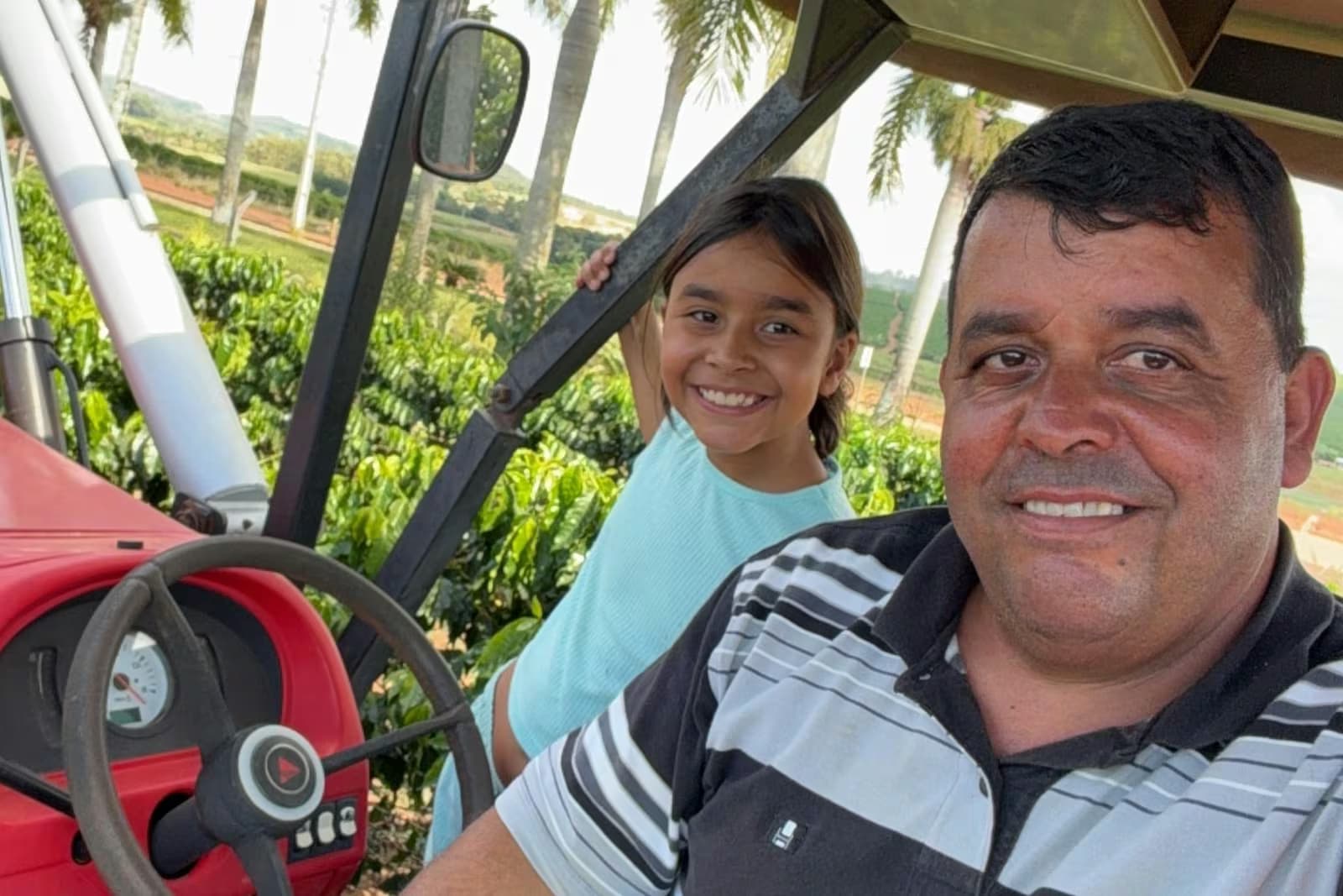 Rony Alexandre Siqueira e a filha sentados no trator, com a lavoura de café do Pontal das Amoras ao fundo.
